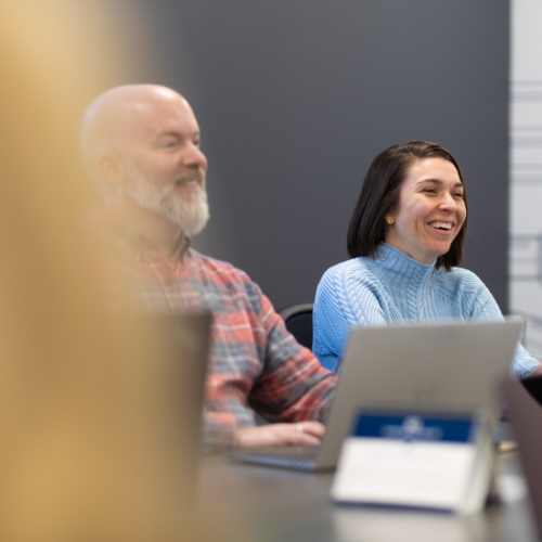 man and woman sitting next to each other at a table with laptops, smiling