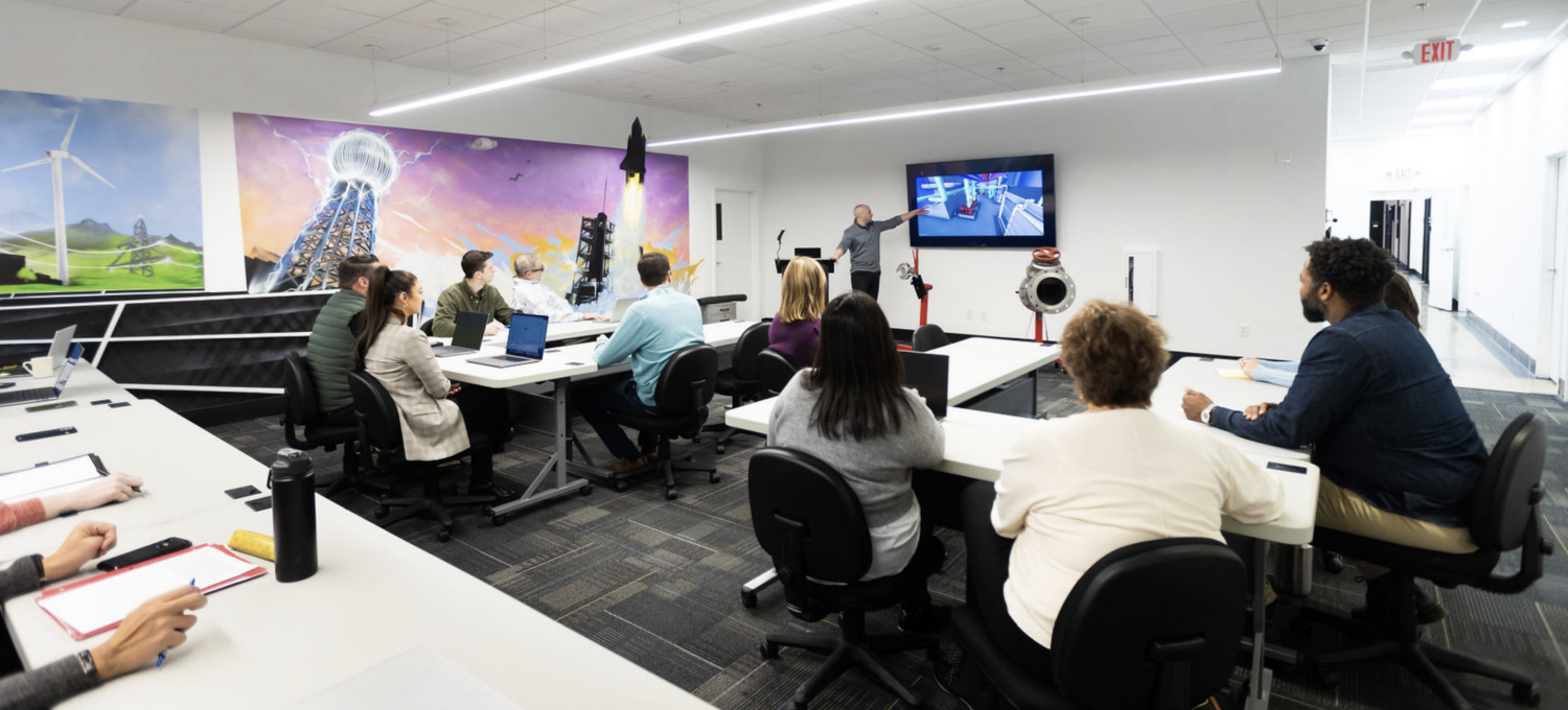 Man pointing to TV while presenting to a room of CDS team members at the office